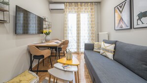 A modern living room with a grey sofa, a dining table with chairs, and a flat-screen TV mounted on the wall. - Elegant Mavili Suite by Cloudkeys (Athens)