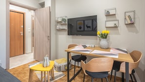 A dining area with a wooden table, chairs, and a vase of yellow flowers. There are wall-mounted shelves with plants and books. - Elegant Mavili Suite by Cloudkeys (Athens)