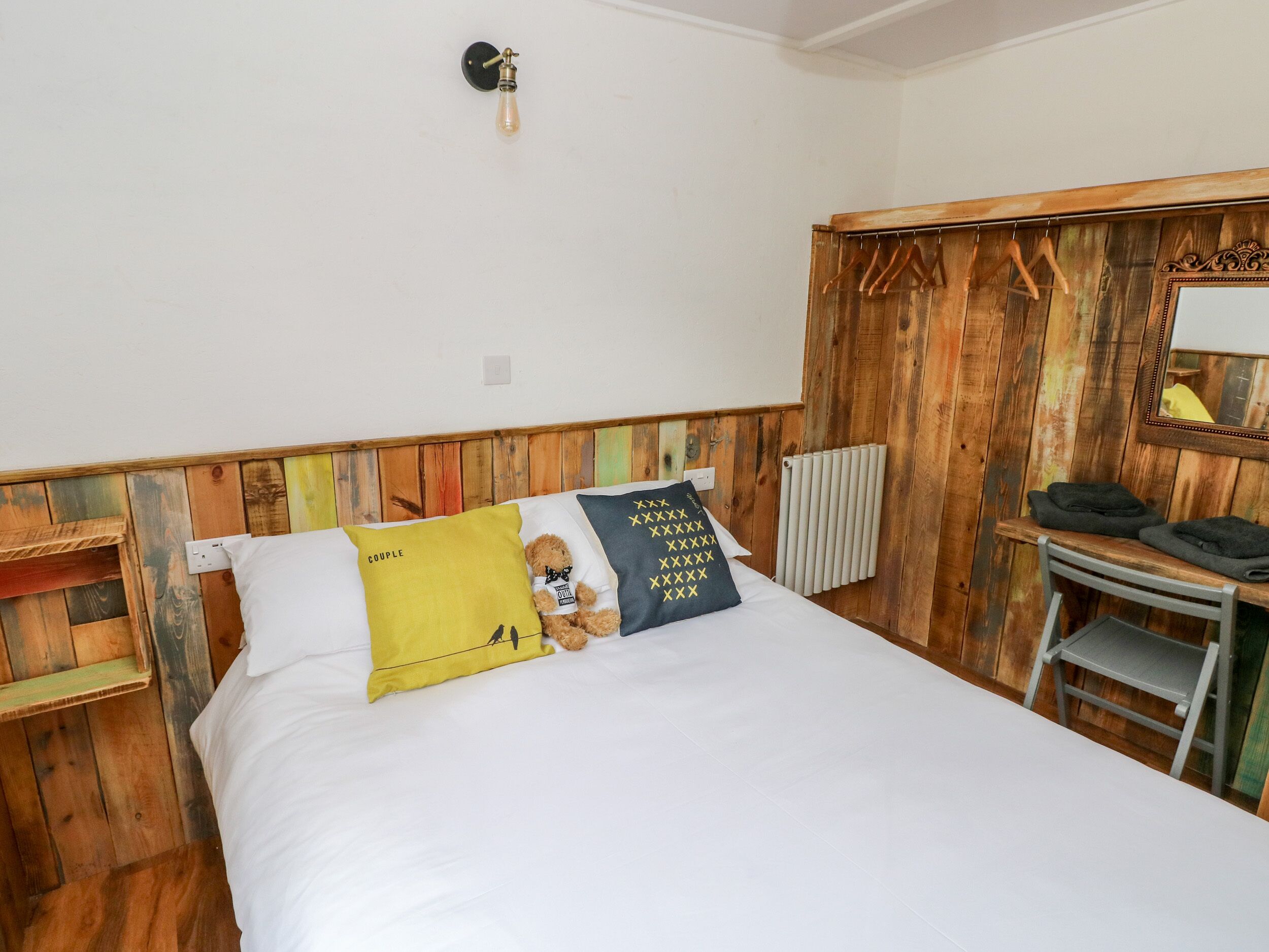 A bedroom with a wooden headboard, a bed with white bedding, a teddy bear, and a mirror on the wall.