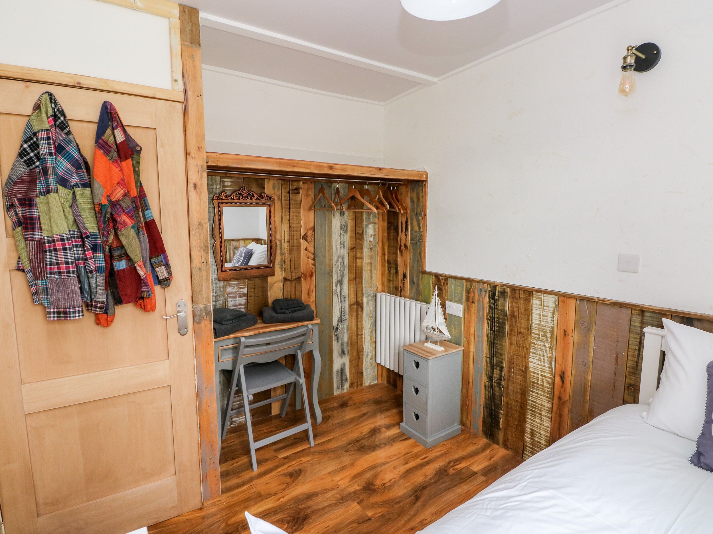 Un dormitorio con piso de madera, una cama, un escritorio con silla, un radiador y un espejo.