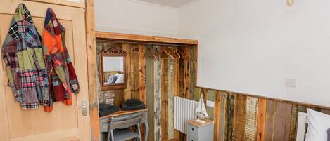 A bedroom with a wooden floor, a bed, a desk with a chair, a radiator, and a mirror.