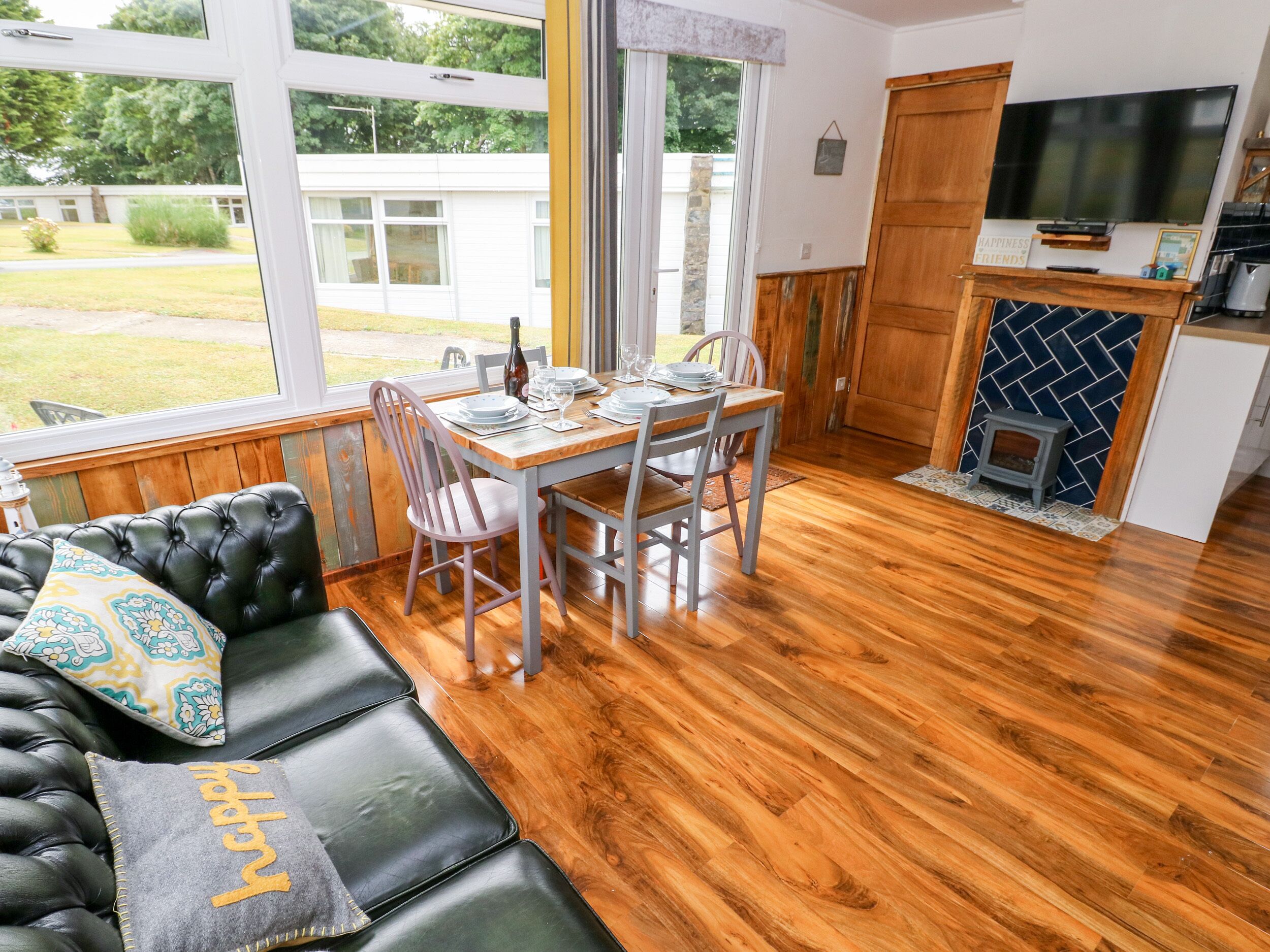 A cozy living room with a leather sofa, a dining table set for four, and a kitchen area with a TV and a small stove.