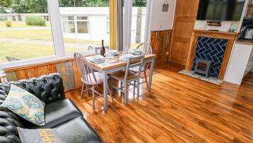 A cozy living room with a leather sofa, a dining table set for four, and a kitchen area with a TV and a small stove.