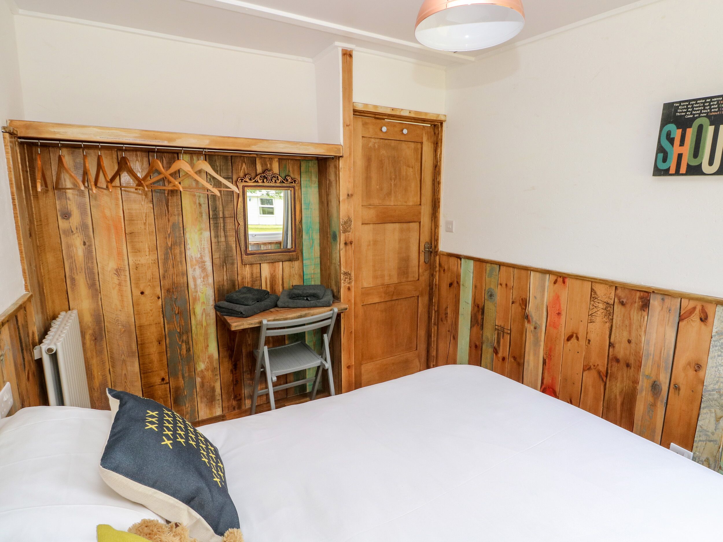 Quarto com guarda-roupa de madeira, pequena escrivaninha com cadeira, radiador e cama com travesseiro.