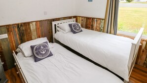 Dos camas individuales con ropa blanca de cama y almohadas a juego, cabeceros de madera y vistas al exterior a través de una ventana.
