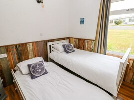 Dos camas individuales con ropa blanca de cama y almohadas a juego, cabeceros de madera y vistas al exterior a través de una ventana.
