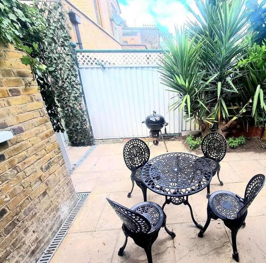 A patio with a round table and four chairs, surrounded by a brick wall and a metal gate.
