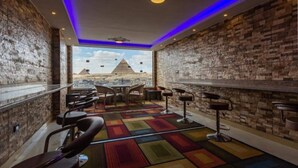 Una stanza con vista sulle piramidi, caratterizzata da un muro in mattoni, un tappeto colorato e sgabelli da bar.