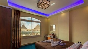 Camera d'albergo con un letto grande, vista sulle piramidi e una lampada a soffitto moderna.