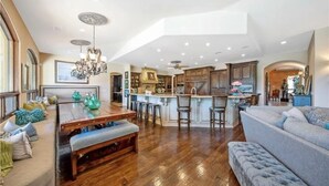 A spacious living area with a wooden dining table, a sofa, and a kitchen with wooden cabinets and a bar area. - Best Choice for Party&Vacation Prestige Big House! (Temecula)
