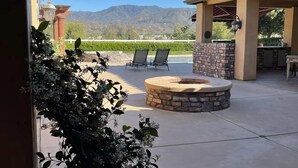 An outdoor patio with a stone fire pit, two lounge chairs, and a view of mountains. - Best Choice for Party&Vacation Prestige Big House! (Temecula)