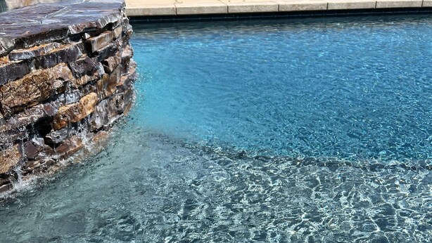 A clear swimming pool with a stone waterfall feature and a stone ledge. - Best Choice for Party&Vacation Prestige Big House! (Temecula)