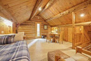 A log cabin interior with a bed, a dining table, and chairs.