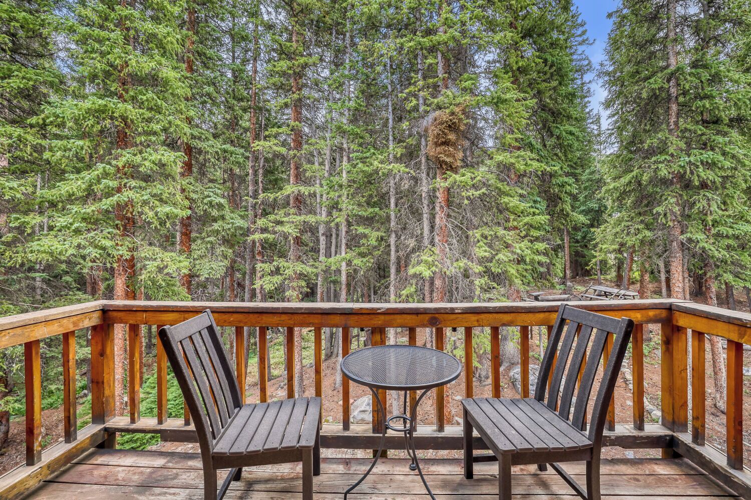 Une terrasse en bois avec deux chaises et une petite table ronde, entourée d’une rambarde, d’où l’on peut admirer une forêt dense.