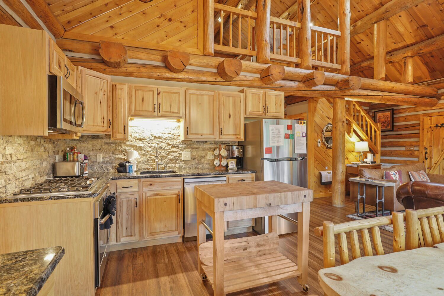 Interior rústico de una cabaña con pisos de madera, una cocina con salpicadero de piedra y un comedor con mesa y bancos de madera.
