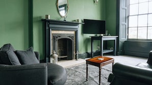 A living room with a fireplace, a television, and a sofa. - Emerald 2BD Retreat in Historic Building, New Town (Edinburgh)