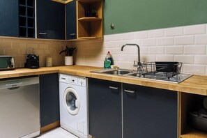A compact kitchen with a dishwasher, a sink with a dish rack, and a coffee maker. - Emerald 2BD Retreat in Historic Building, New Town (Edinburgh)