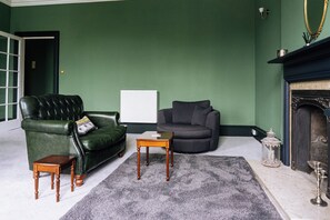 A room with a green wall, a leather sofa, a grey armchair, a small wooden table, and a fireplace.