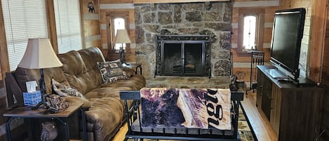 Una sala de estar acogedora con chimenea de piedra, sofá de cuero y televisor sobre un mueble de madera.