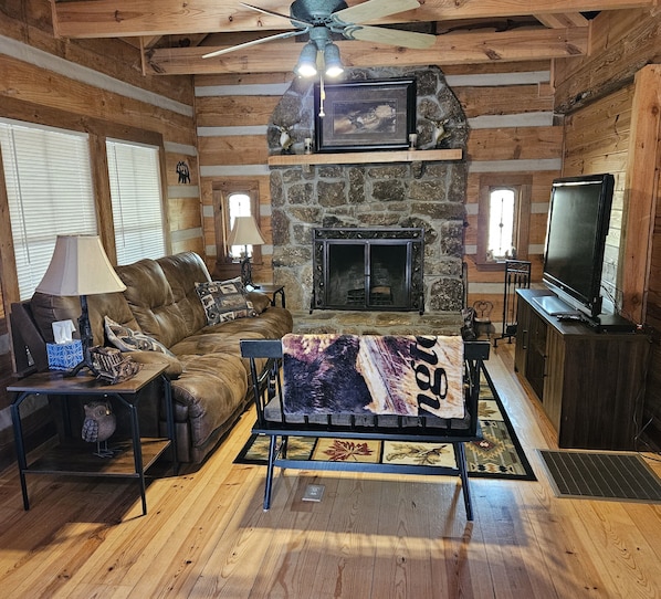 A cozy living room with a stone fireplace, leather sofa, and a television on a wooden stand. - THE WOODLANDS - VERY QUIET SECLUDED CABIN (Mentone)