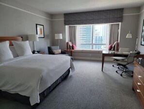 A hotel room with a large bed, a desk, a chair, a lamp, and a window with a view of buildings. - Four Seasons Studio - Privately Owned Unit (Miami)