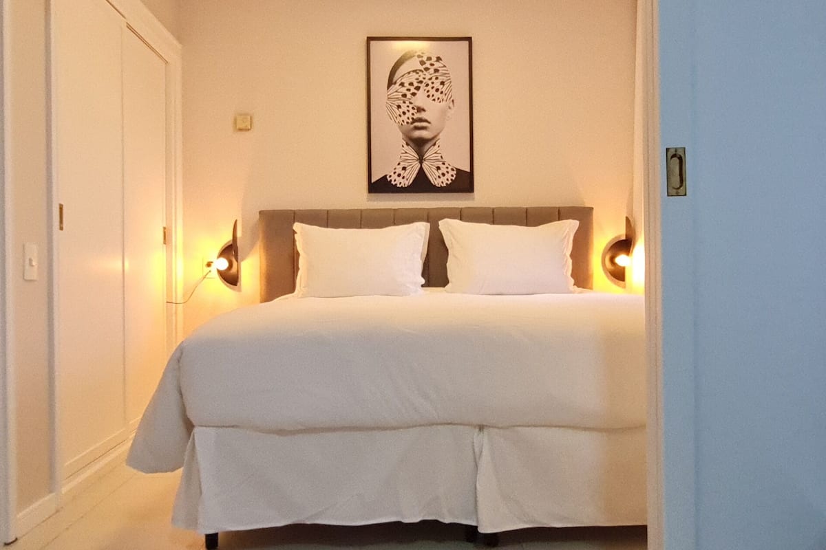A hotel room with a large bed, two bedside lamps, a headboard, and a framed artwork on the wall.
