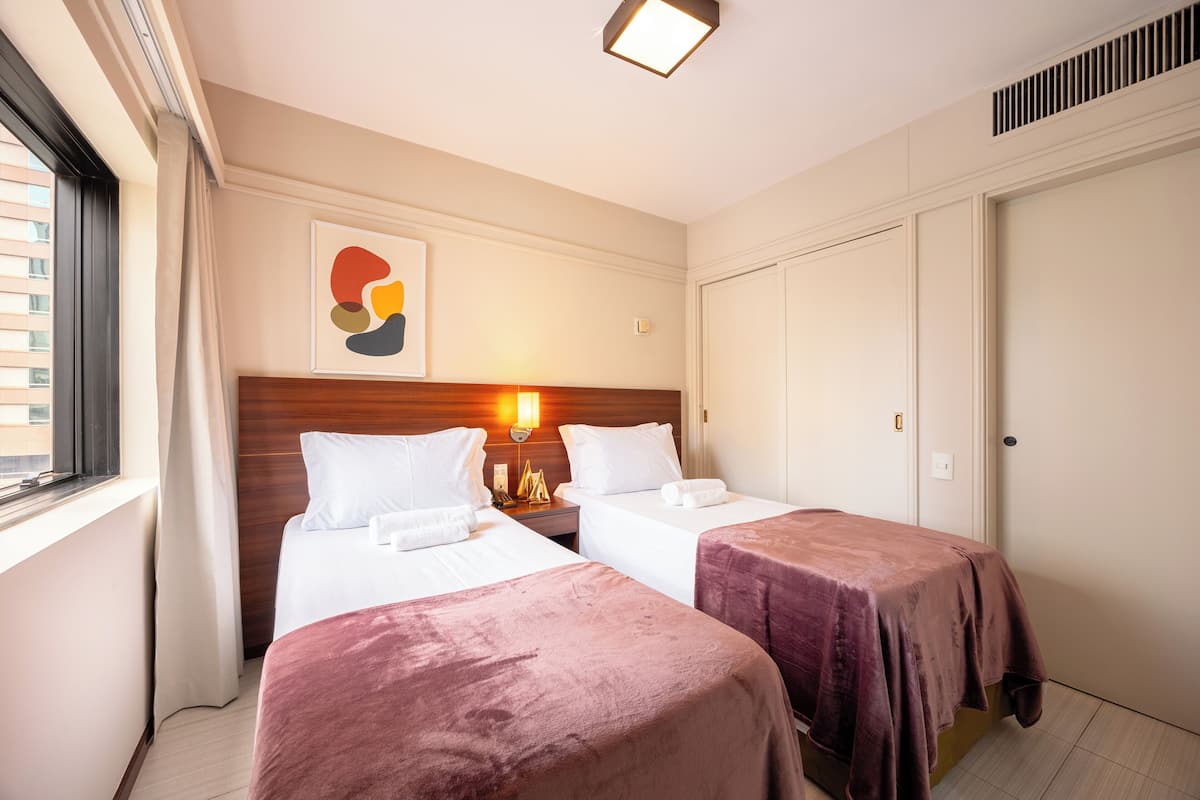 A hotel room with two beds, a wooden headboard, a wall-mounted light, and a door.