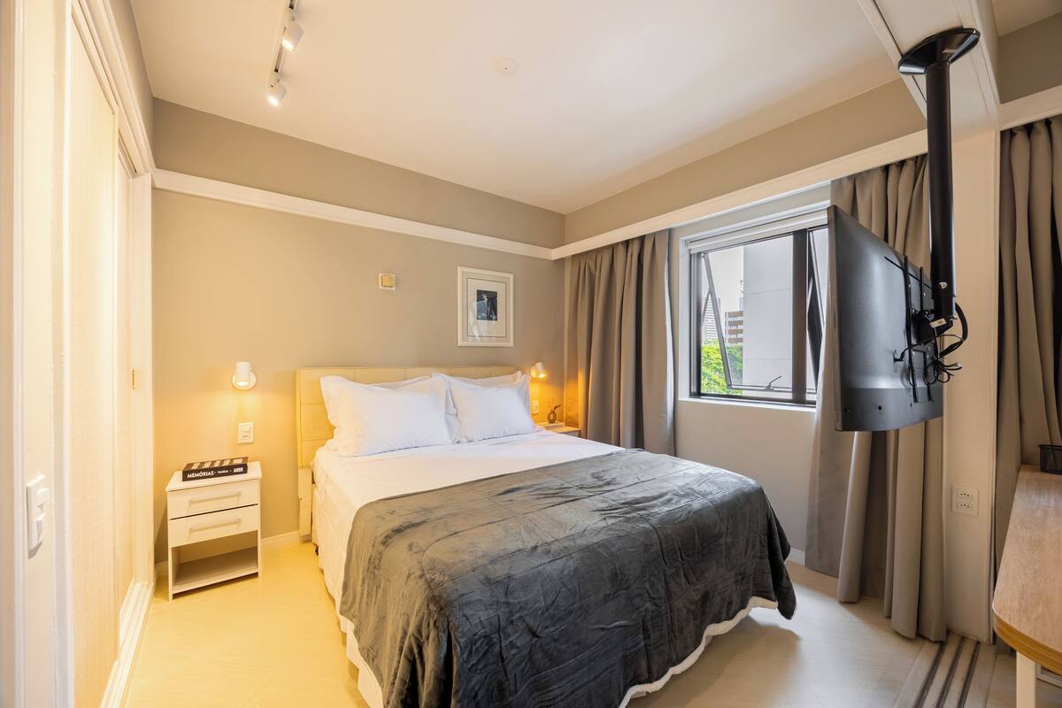 A bedroom with a bed, bedside tables, a TV, and a window with curtains.
