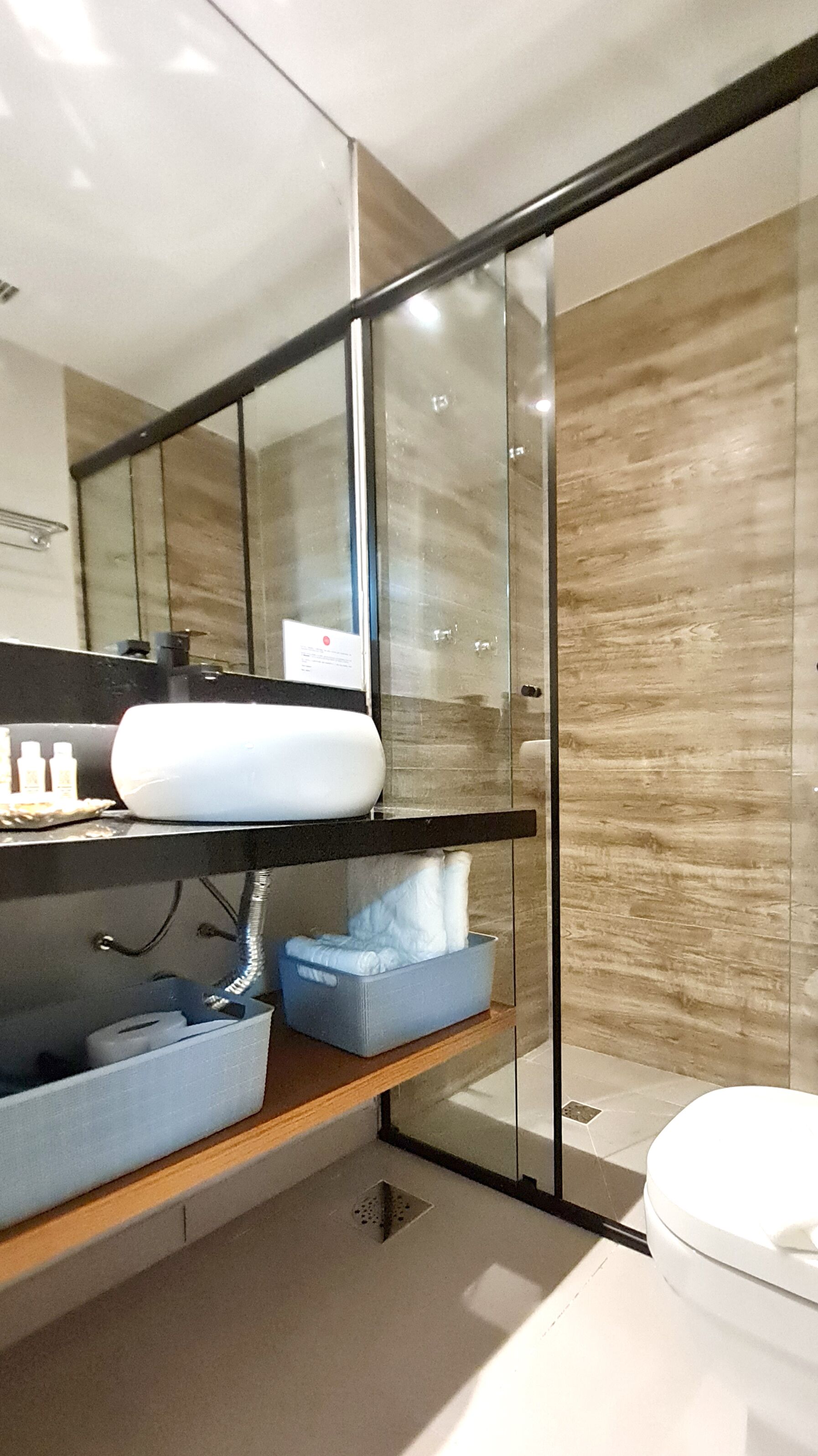 A modern bathroom with a glass shower enclosure, a wooden vanity, and a white sink.
