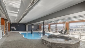 Ein Hallenbad mit Whirlpool, Steinwänden und großen Fenstern.