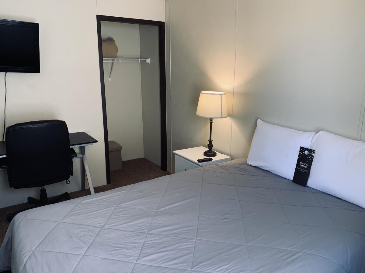 Ein Hotelzimmer mit Bett, Schreibtisch, Stuhl, Nachttisch mit Lampe und Spiegel.