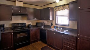 A kitchen with dark wooden cabinets, a stainless steel refrigerator, a microwave, a stove, a dishwasher, and a window with curtains. - Ellipse Global Lodge (Carlsbad)