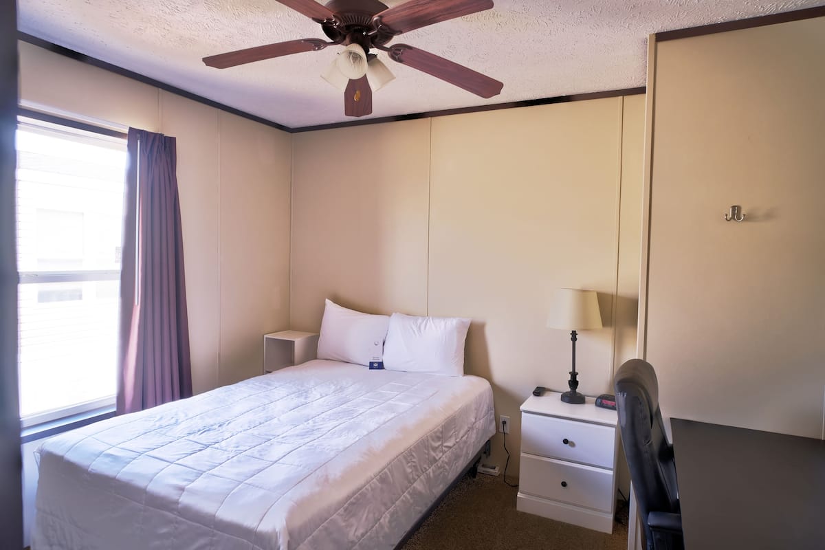 A hotel room with a bed, bedside table, lamp, and a ceiling fan.