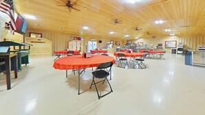 A spacious indoor area with multiple tables and chairs, wooden walls, and ceiling fans. - Ellipse Global Lodge (Carlsbad)