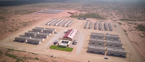 An aerial view of a large, rectangular parking lot with multiple rows of parked vehicles and a central building with a red roof.