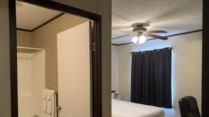 A bedroom with a bed, a chair, a ceiling fan, and a window with curtains. - Ellipse Global Lodge (Carlsbad)
