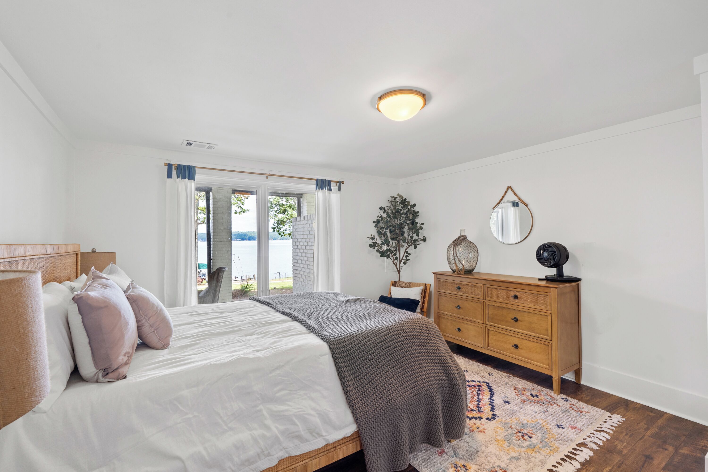 Un dormitorio con cama, cómoda, espejo y vistas al exterior.