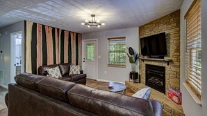 A living room with a stone fireplace, leather sofa, and a television mounted on the wall.