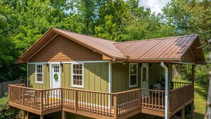 A two-story wooden cabin with a balcony on the upper floor, surrounded by trees.
