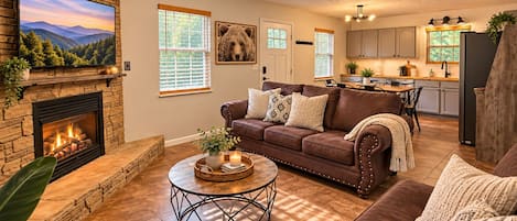 A living room with a fireplace, a brown leather sofa, a round coffee table, and a television mounted on a stone wall.