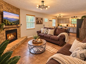 A living room with a fireplace, a brown leather sofa, a round coffee table, and a television mounted on a stone wall.
