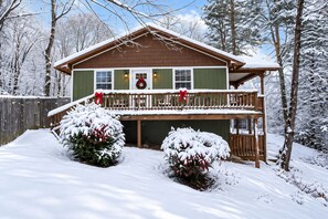 A two-story cabin with a covered porch, surrounded by snow-covered trees.