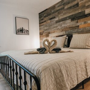 Un dormitorio con cabecera de madera, un cuadro enmarcado en la pared y una cama con colcha y dos almohadas con forma de cisne.