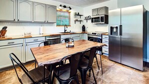 A modern kitchen with a wooden dining table, black chairs, a stainless steel refrigerator, and a built-in oven.