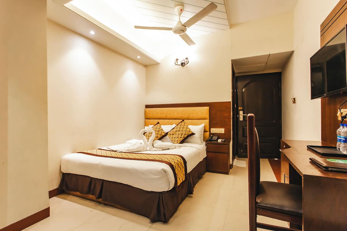 A hotel room with a bed, a desk, a chair, a ceiling fan, a TV, and a door.