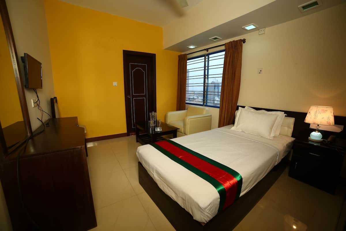 A hotel room with a bed, a desk, a chair, a nightstand, and a window with curtains.