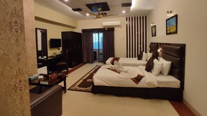 A hotel room with two beds, a desk, a TV, and a ceiling fan. - Central Inn (Dhaka)