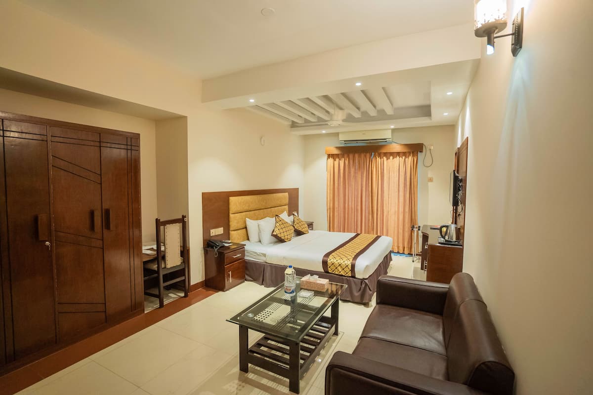 A hotel room with a bed, a sofa, a glass coffee table, a wardrobe, and a desk with a chair.