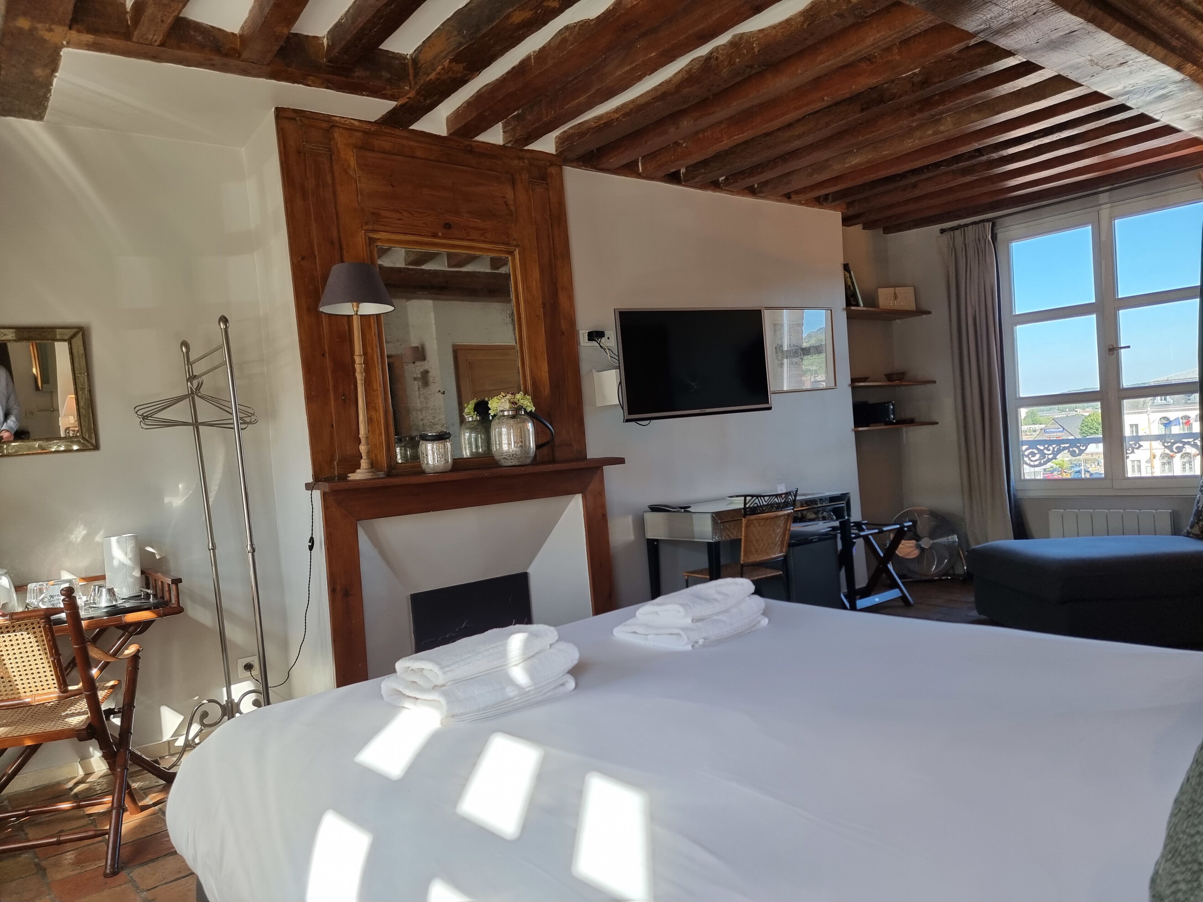 Een hotelkamer met een groot bed, een bureau met stoel, een televisie en een raam met uitzicht op gebouwen.