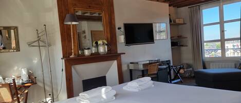 Een hotelkamer met een groot bed, een bureau met stoel, een televisie en een raam met uitzicht op gebouwen.